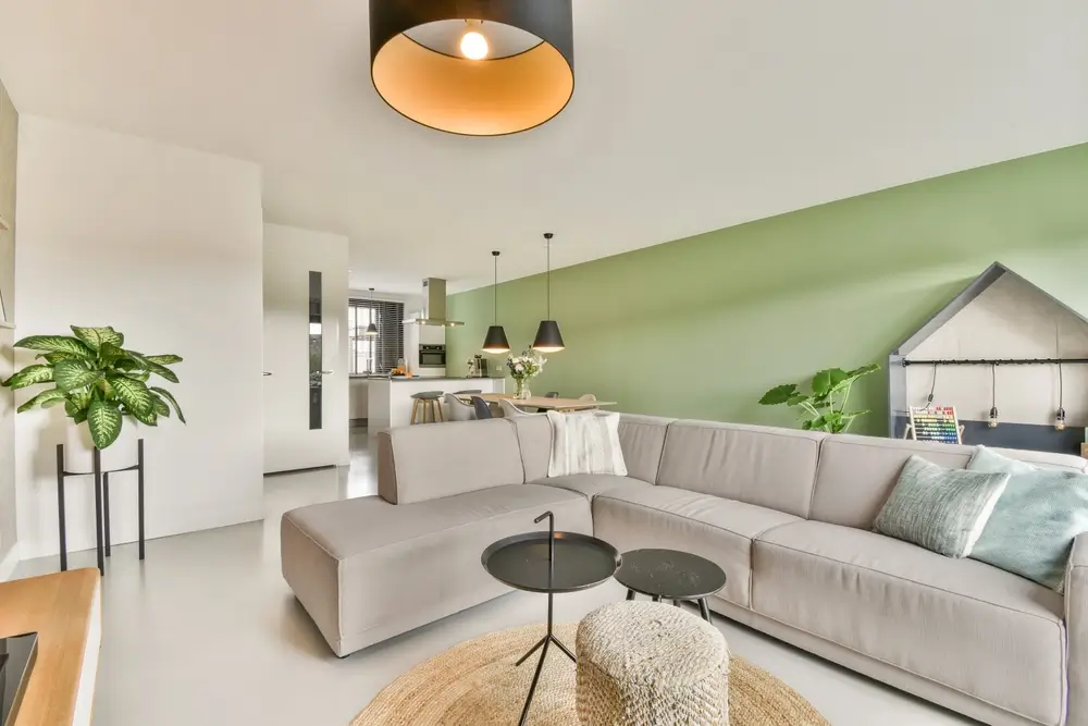 Un salon élégant avec un canapé gris clair, un éclairage original et un mur d'accent vert, créant une atmosphère paisible et moderne propice à la détente.